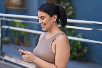 Wall Mural - Young beautiful hispanic woman smiling confident using smartphone at street