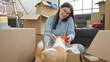 © Krakenimages.com - Young hispanic woman with chihuahua dog speaking on the phone unpacking cardboard box at new home