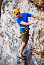 A Young Man In A Blue Shirt And Yellow Helmet Rock Climbs On A Sandstone Cliff In Tennessee