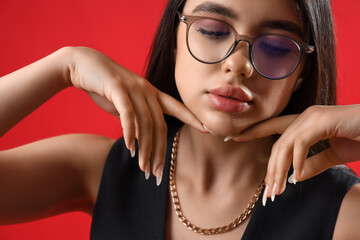 Wall Mural - Fashionable young woman wearing glasses on red background