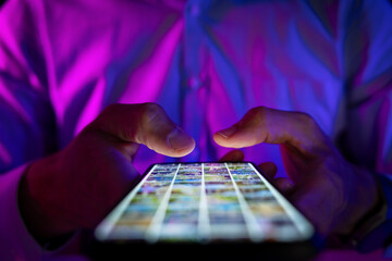 man scrolling mobile phone screen in dark room with neon lights. internet browsing, social media and