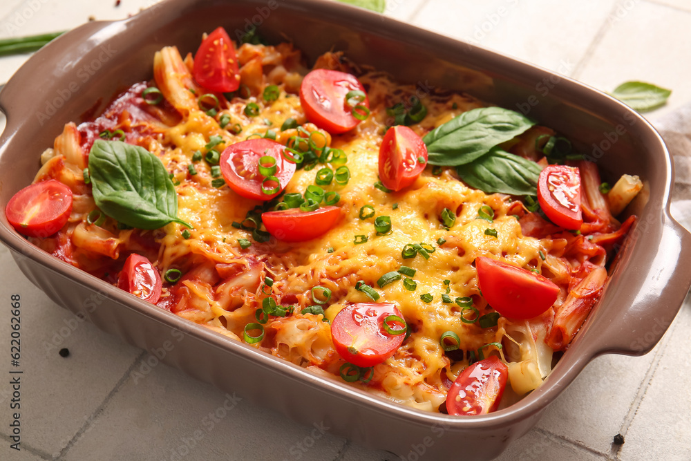 Baking dish of pasta with tomato sauce and cheese on white tile background