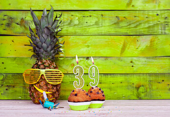 Creative card postcard happy birthday with number  39. Background character pineapple in festive glasses. Copy space anniversary card on yellow colorful wooden background.