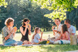 © Soloviova Liudmyla - Big family sitting on the picnic blanket in city park during weekend Sunday sunny day. They are smiling, laughing and eating boiled corn and watermelon. Family values and outdoors activities concept.