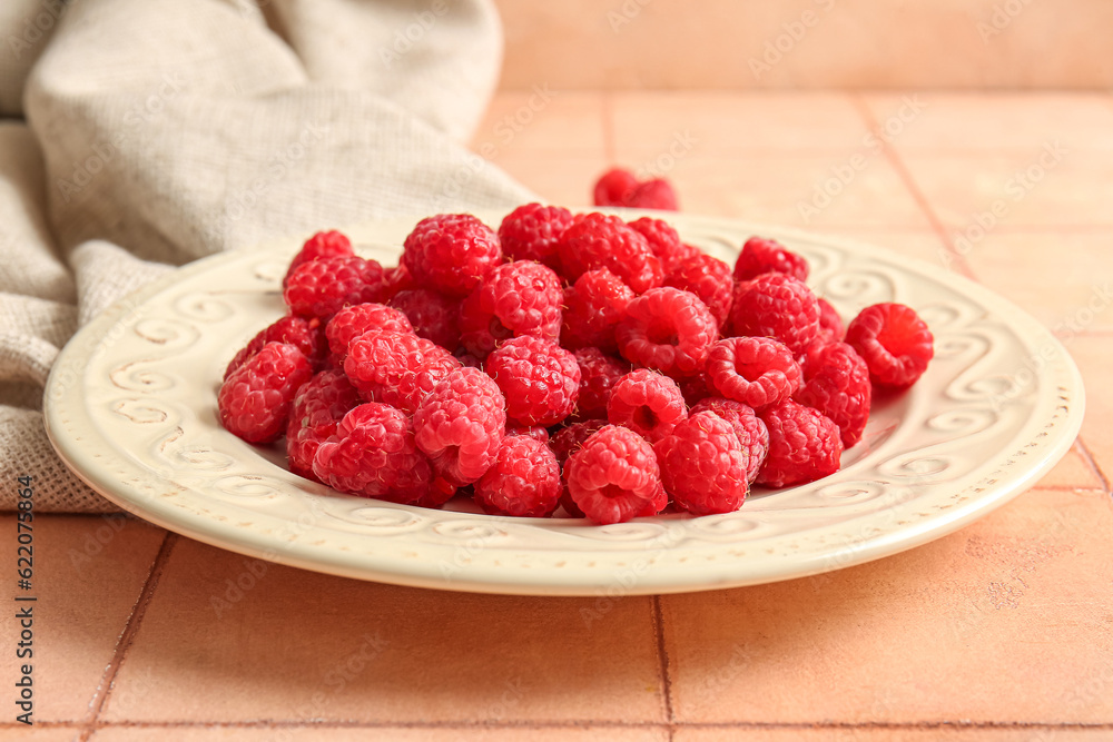 Plate with fresh raspberries on pink tile background