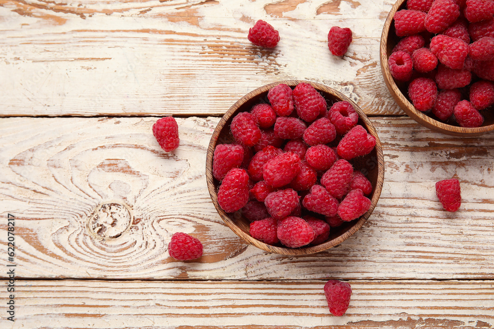 Bowls with fresh raspberry on light wooden background