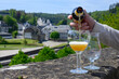 Pouring of blond strong Belgian abbey beer in to glass in sunny day with nice view on old town Bouillon, Belgium
