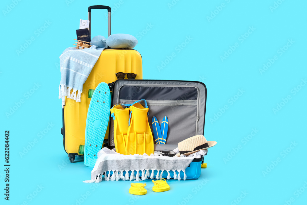 Suitcases with skateboard and different beach accessories on blue background. Travel concept