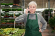 © JackF - Focused senior woman garden shop owner having phone conversation, discussing supply of ornamental potted plants from greenhouses for sale