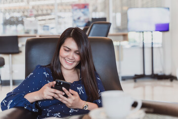 Canvas Print - Smiling asian woman sitting on couch at office using smartphone. Beautiful asian use internet on phone for business.