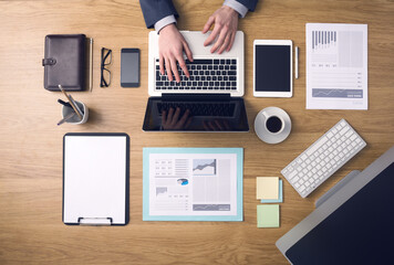 Businessman working on a laptop at office desk with paperwork and other objects around, top view