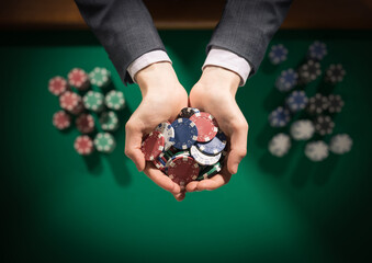 Elegant male casino player holding a handful of chips with green table on background, hands close up top view