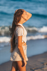 Wall Mural - Adorable young girl with beautiful long hair enjoy tropical beach vacation. The girl on the seashore at sunset