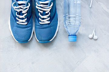 Wall Mural - Flat lay sport shoes, bottle of water and earphones on gray concrete background. Concept healthy lifestyle, sport and diet. Focus is only on the sneakers.