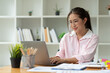 © Phimwilai - Confident Asian businesswoman using laptop computer working in office with calculator papers on table make a plan analyzing financial reports business plan investment analytical concept.