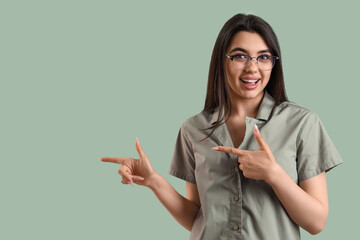 Wall Mural - Beautiful young woman wearing glasses and pointing at something on color background