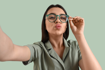 Wall Mural - Beautiful young woman wearing glasses and taking selfie on color background