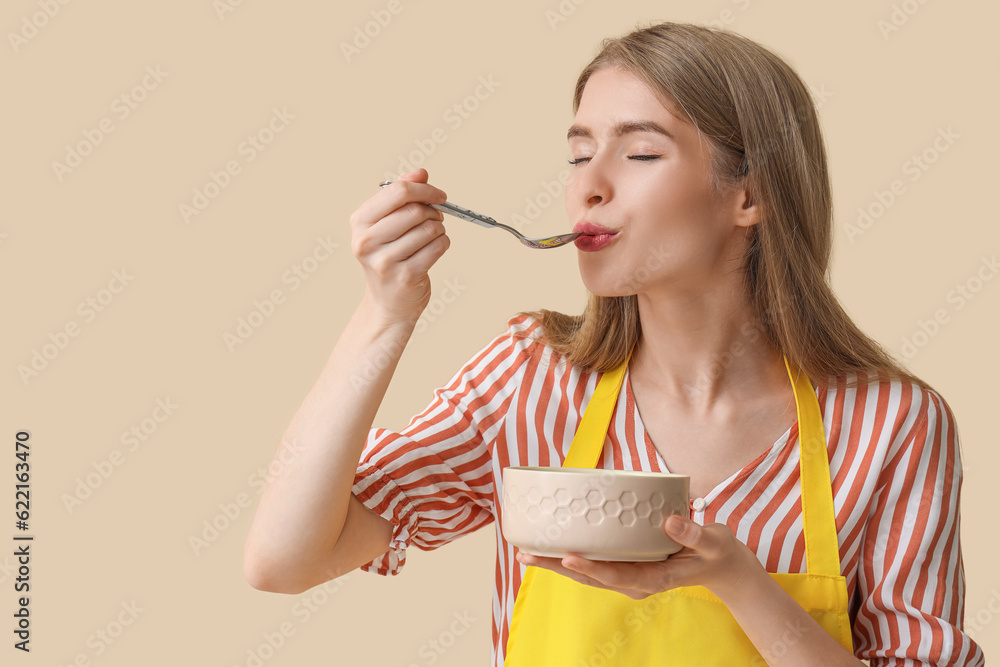Young woman with spoon and bowl on beige background
