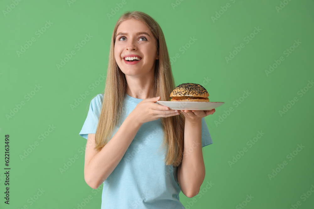 Young woman with tasty burger on green background