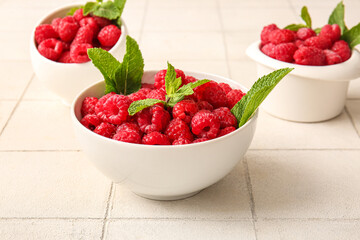 Bowls with fresh raspberries and mint on white tile background