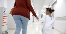 African American Mother And Daughter In Hospital Gown Holding Hands Walking In Corridor, Slow Motion