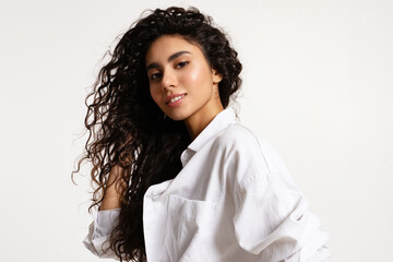 Wall Mural - Beautiful smiling young modern woman with curly bouffant long hair wearing white oversize shirt on white background