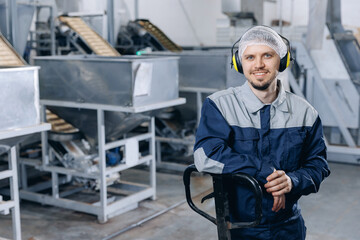 Wall Mural - Man loader in uniform holding trolley with bags of wheat, nuts in warehouse. Industrial manufacturing factory coffee beans