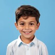 Portrait of a smiling little boy with brown hair. Closeup face of a handsome  small kid smiling at the camera on a blue background. Front view, happy male Arab child in a white shirt.
