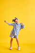 © master1305 - Full-length portrait of beautiful little child, girl listening to music in headphones and dancing against yellow studio background. Concept of emotions, childhood, education, fashion, lifestyle, ad