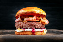 A Large Burger With A Meat Patty, Fried Bacon, Crispy Onions, Cottage Cheese And Cranberry Sauce On A Wooden Board.
