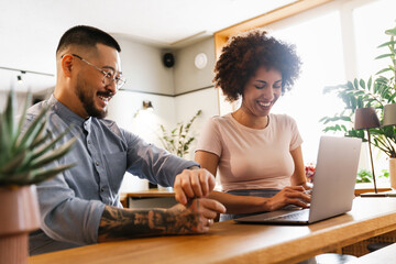 Wall Mural - Two smiling business owners using laptop while working in cafe