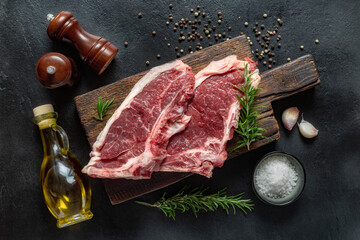 Canvas Print - Fresh beef raw steak on wooden board with spices on dark stone background top view