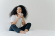 Afro woman's cozy morning: sips hot drink in bed, content gaze, comfy attire, sunny weather, white wall.