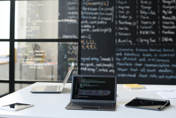 Workplace of IT teacher with laptop with codes on the screen and blackboard in the background
