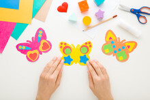Young Adult Woman Hands Holding Colorful Butterfly Shape From Paper On White Table Background. Pastel Color. Making Decoration Elements. Closeup. Point Of View Shot. Top Down View.