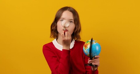Stylish smiling school teenage girl holding magnifying glass in her hand and look on globe