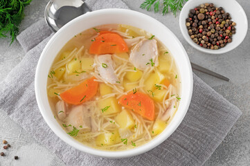 Wall Mural - Chicken soup with noodles and vegetables in white bowl on a gray concrete background.