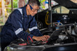 © Surachai - Close-up view of auto mechanic using technology working on car engine in garage. Repair service.