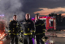 Brave Firefighters Team Walking To The Camera. In Background Paramedics And Firemen Rescue Team Fight Fire In Car Accident, Insurance And Save Peoples Lives Concept.