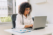 © Renata Hamuda - hispanic female doctor in glasses with stethoscope typing on computer while sitting at table in modern clinic