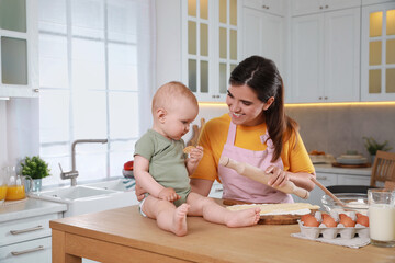 Wall Mural - Happy young woman and her cute little baby cooking together in kitchen