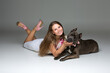 © Designpics - Beautiful elegant happy young woman in white dress hugging adult grey amstafford terrier dog with bow on neck. Studio shot over grey background. Copy space.