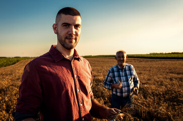 Wall Mural - Portrait of two farmers standing in golden wheat field at sunset.