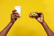 © Богдан Маліцький - african american man's hands hold delicious fresh burger and paper cup coffee on yellow isolated background