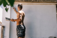 Unrecognizable Shirtless Young Man Painting Wall With Brush In Daylight