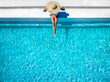 © moofushi - Aerial overhead view of a woman in a bathing suit and sunhat sitting on a pool edge with copy space, summer holiday travel concept