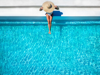 aerial overhead view of a woman in a bathing suit and sunhat sitting on a pool edge with copy space,