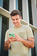 © Jose Calsina - Vertical portrait of happy teenager male smiling and typing on a smart phone using a social media app outdoors. Young man having fun texting messages on a cellphone. Handsome guy using a mobile phone