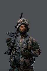 Confident soldier in NATO uniform and helmet poses with his rifle on a plain grey background, showcasing the courage and strength of military personnel