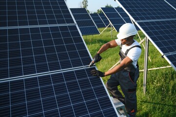 Portrait of african american electrician engineer in safety helmet and uniform installing solar panels.